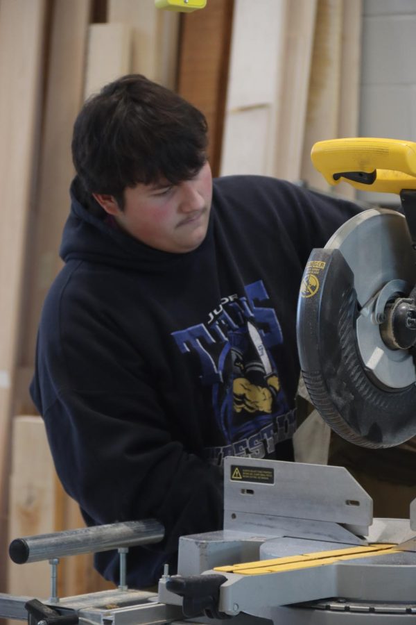 Mikey Bonge, 12th, student-aid in a trades class, attaching a cover to the table saw. He’s been in trade classes all four years in high school and has helped the school with many projects like building sheds, book shelves, benches, and more. 