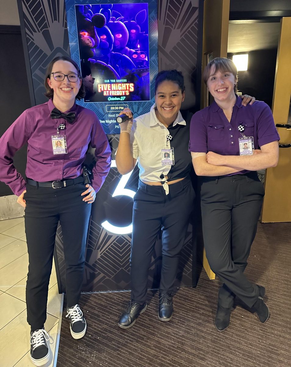 Sebastian Spaz Woodworth (Papio South graduate, UNL alumni. Right), Rachel Grossnickle (Bellevue West High graduate, MCC alumni. Left), and me (center) in FNaF security guard costumes in front of movie poster at B&B theaters.
